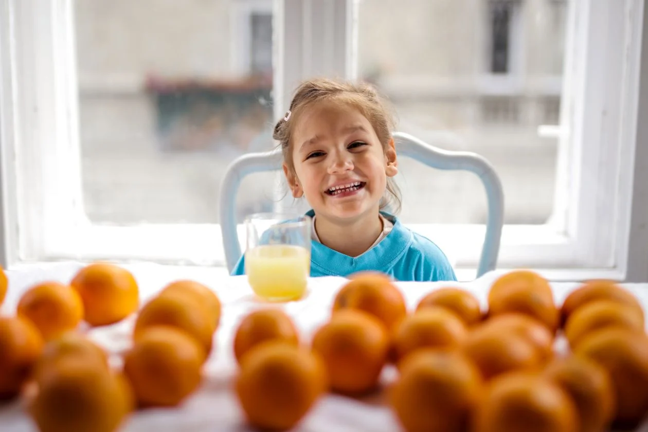 A cheerful young girl smiling at a table with oranges and orange juice