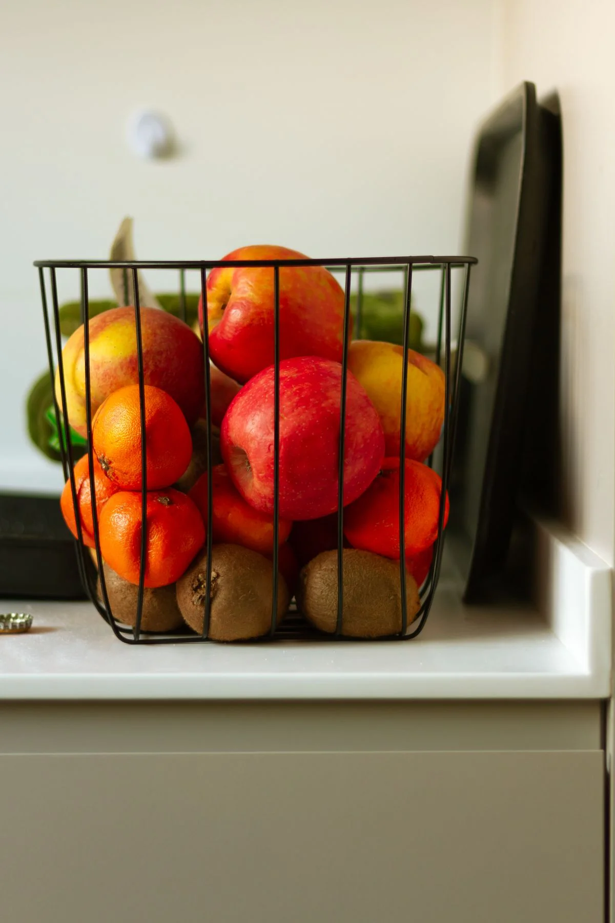 An open wire basket holding apples, oranges, and kiwis on a counter