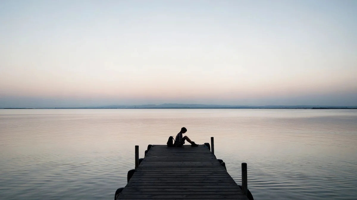 A person sitting alone on a dock at sunset over a calm sea, a peaceful moment of solace
